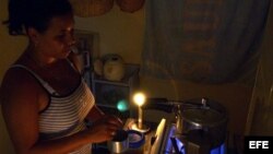 Una mujer prepara unos platos de comida en la cocina, iluminada con velas, en un apagón en el barrio de Alamar