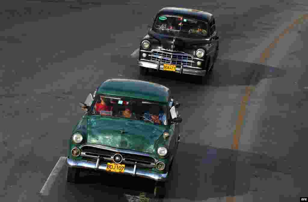 Dos autos antiguos que funcionan como taxis privados circulan por una calle habanera.