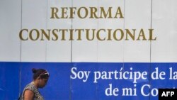 Una cubana camina frente a un poster donde se anuncia la reforma Constitucional.