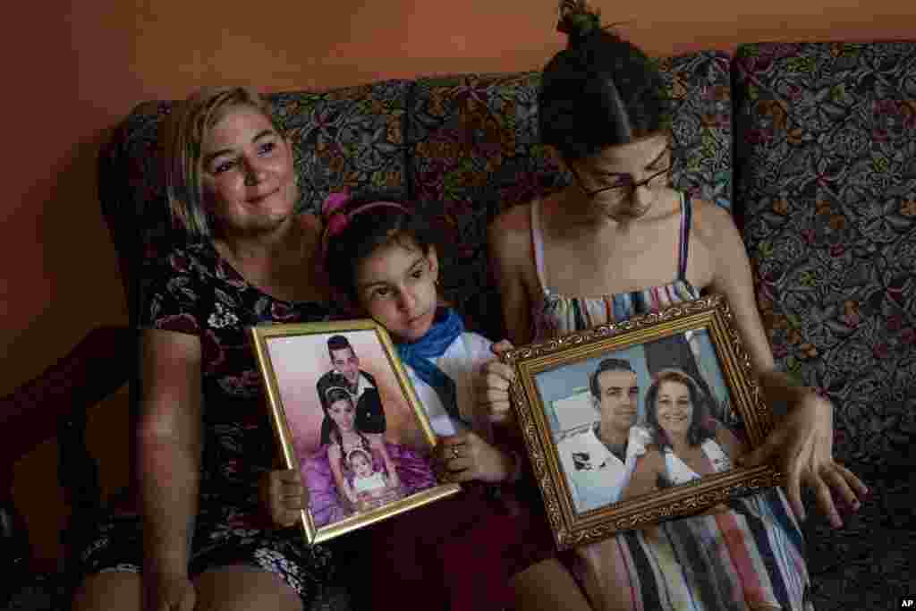 Danmara Triana (izquierda), con sus hijas Alice (centro) y Claudia, muestran fotos suyas con su hermano y su padres, quienes se mudaron a Estados Unidos en 2015. (AP Foto/Ramón Espinosa)