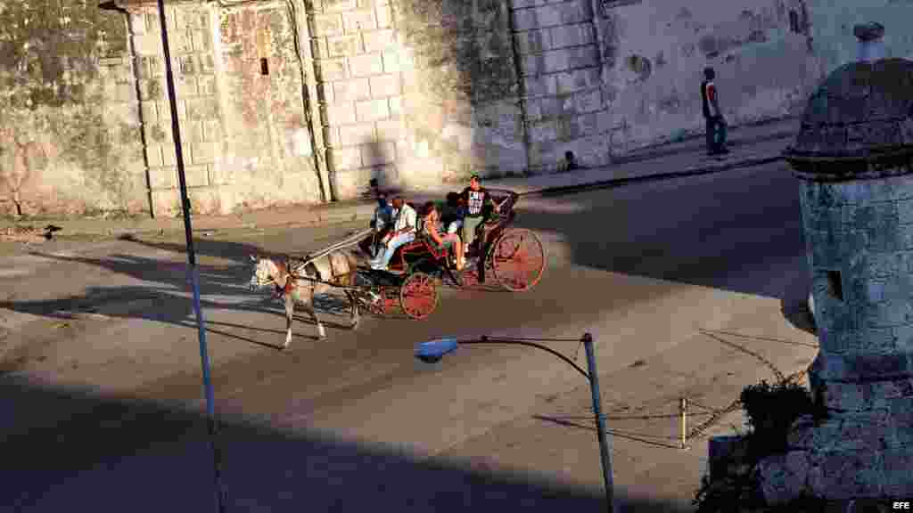 Varios turistas pasean en un coche de caballos por una avenida de La Habana Vieja.