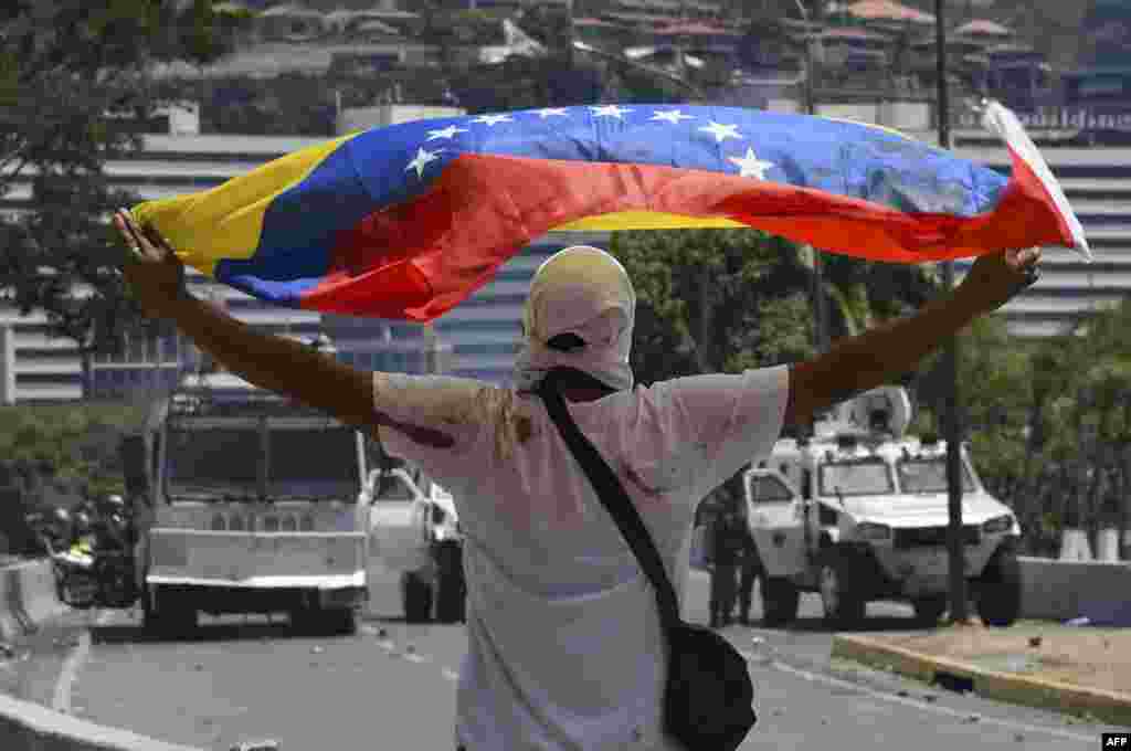 Un partidario del presidente interino de Venezuela, Juan Guaido, muestra una bandera nacional frente a las tanquetas del ejército.