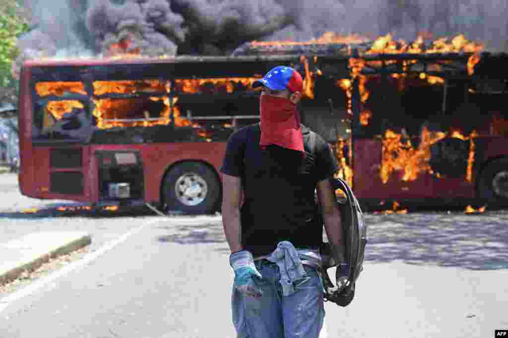 Un manifestante de la oposición camina cerca de un autobús en llamas durante los enfrentamientos con soldados leales a Nicolás Maduro.