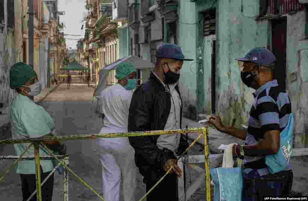 Un residente muestra su identificación a un oficial de policía que está limitando el acceso a un vecindario como una forma de frenar la propagación de la pandemia de COVID-19, 22 de febrero de 2021. (AP Foto/Ramon Espinosa)